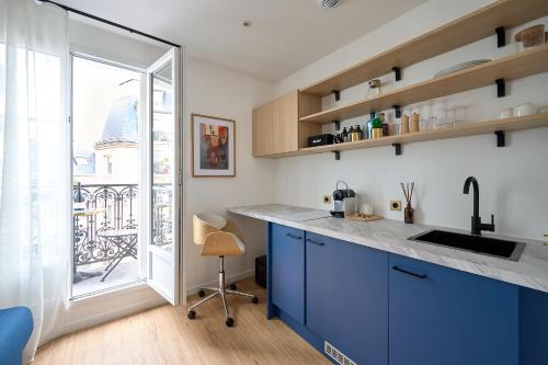 une cuisine avec des placards bleus et une grande fenêtre dans l'établissement Studio design tout équipé avec balcon, à Paris