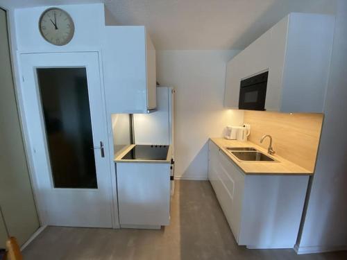 a small white kitchen with a clock on the wall at Le Chalain cosy proche centre ville in Les Rousses