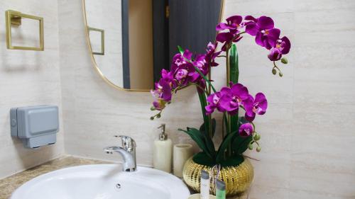 a bathroom sink with a vase with purple flowers in it at Studio Apartment in Abudhabi Zc in Abu Dhabi