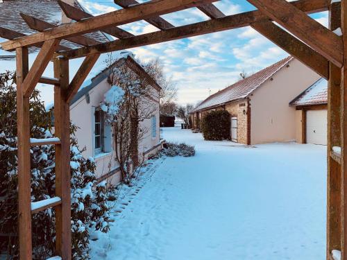 a snow covered yard with a wooden pergola at Gîte de L'Oliviade - Campagne & Confort in Billancelles