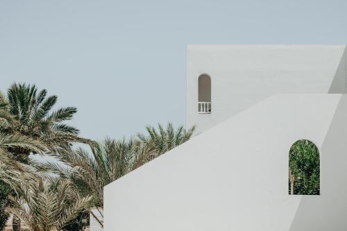 a white building with a window and palm trees at Hotel Bougainvillier Djerba in Taguermess