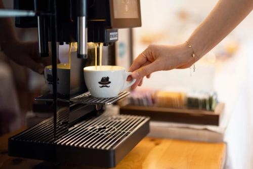 a person is holding a coffee cup on a coffee machine at Weingarten Terlan - Rooms & Breakfast in Terlano