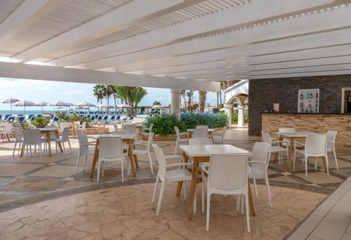 un patio con mesas y sillas blancas y el océano en VOI Praia de Chaves Resort en Sal Rei