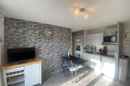 Il comprend une cuisine dotée d'un mur en briques et d'une télévision. dans l'établissement Bright T2 with balcony - close to the sea, à Ouistreham
