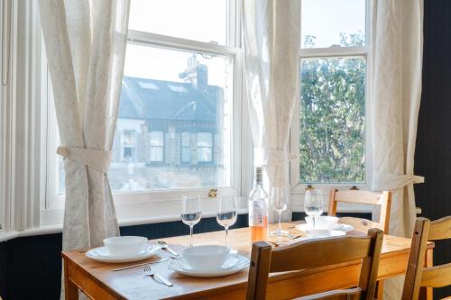 uma mesa de madeira com copos e pratos ao lado de uma janela em 4 bedroom Stunning Flat Near Westfield & Trains em Londres