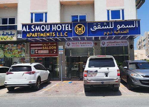 Al Smou Hotel Apartments - MAHA HOSPITALITY GROUP في عجمان: سيارتين بيض متوقفتين امام مبنى