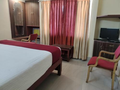 a bedroom with a bed and two chairs and a television at Hotel Vyshak International in Mysore