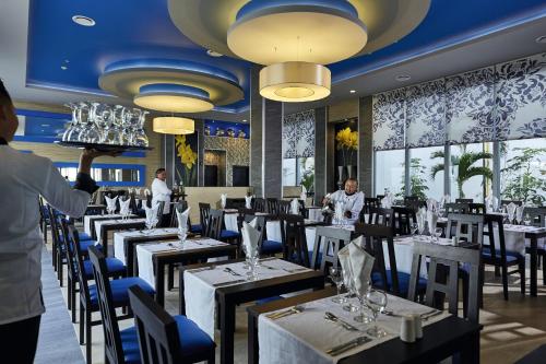 a restaurant with black tables and blue chairs and a waiter at Riu Dunamar - All Inclusive in Cancún