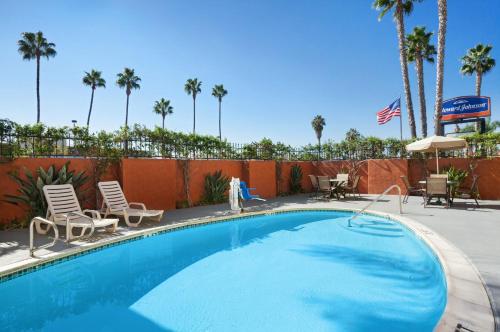 a swimming pool with chairs and a fence and palm trees at Howard Johnson by Wyndham San Diego Sea World in San Diego