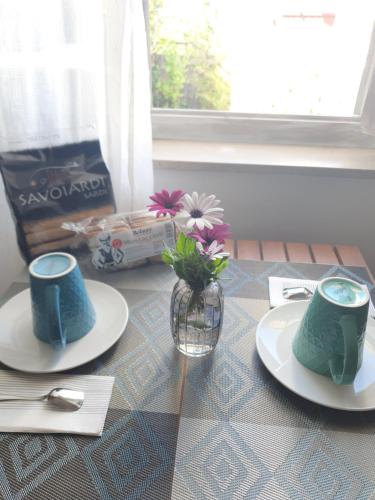 a table with two plates and a vase with flowers on it at Sulla via del Mare Room I.U.N R5045 in Terralba
