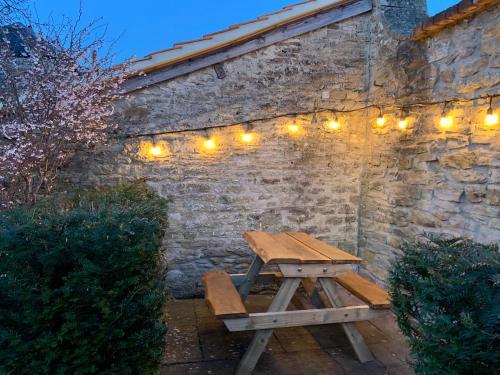 Romantic Little House near Bath في Rode: طاولة نزهة خشبية على جدار من الطوب مع أضواء