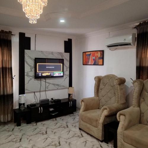 ein Wohnzimmer mit 2 Stühlen und einem Flachbild-TV in der Unterkunft J Lounge in Ikorodu
