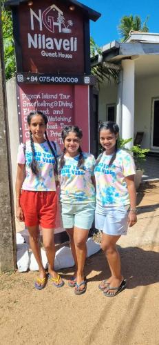 three girls are standing in front of a sign at Nilaveli Guest House in Nilaveli