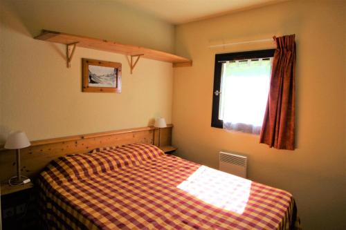 a bedroom with a bed with a checkered blanket and a window at Chalets Du Thabor - 2 Pièces pour 4 Personnes 82 in Modane