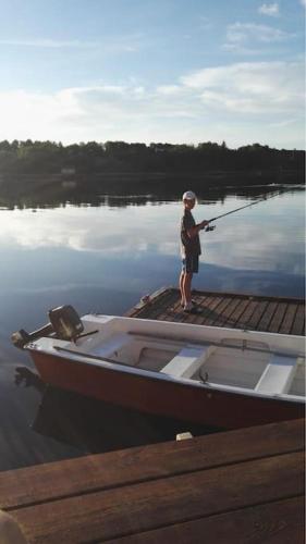 a person standing on a dock with a boat on the water at Feriehus og naust i idylliske omstendigheter in Tjørvåg