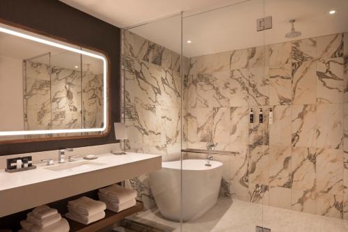 a bathroom with a shower and a sink and a tub at Caesars Republic Scottsdale, a Hilton Hotel in Scottsdale