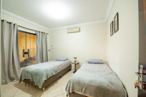two beds in a white room with a window at Pousada no coração de Londrina in Londrina