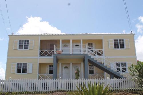 uma casa amarela com uma cerca branca à frente. em Petals Lovely Beach Villa em Saint Johnʼs