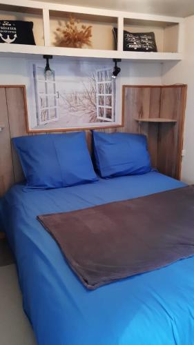 - un lit avec des oreillers bleus et une tête de lit en bois dans l'établissement Mobil home avec terrasse camping du gouffre numéro 88 plougrescant, à Plougrescant