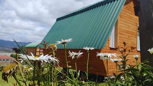 a wooden house with a green roof and flowers at El Alpino Cabaña Glamping & Camping in Guatavita