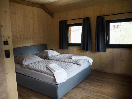 a bed in a wooden room with two windows at Zwiesler Haus Bschlabs in Bschlabs