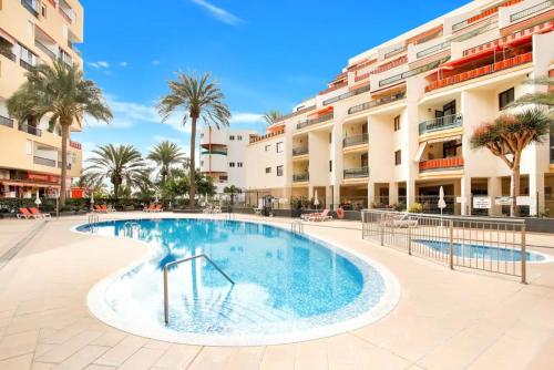 a swimming pool in front of a building with palm trees at Royal View Apartment - Los Cristianos in Los Cristianos