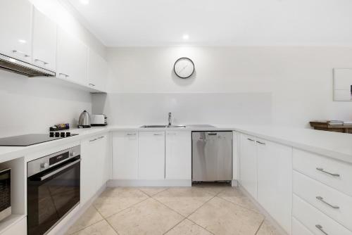 a kitchen with white cabinets and a clock on the wall at Oceanique in Coffs Harbour