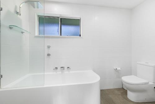 a white bathroom with a tub and a toilet at Oceanique in Coffs Harbour