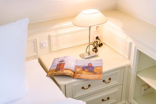 a bedside table with a book and a lamp on it at Avenarius Hüs in Kampen