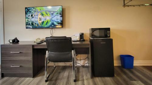 a desk with a computer and a chair and a television at Maple Leaf Inn & Suites in Kincardine