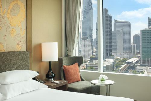 a bedroom with a bed and a chair and a window at Eastin Grand Hotel Sathorn in Bangkok