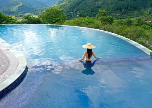 a woman in a hat sitting in a swimming pool at Le Champ Tu Le Resort Hot Spring & Spa in Yen Bai