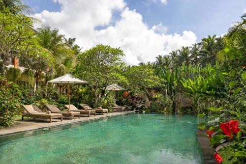 a pool with chairs and umbrellas in a resort at The Kalyana Ubud Resort in Ubud