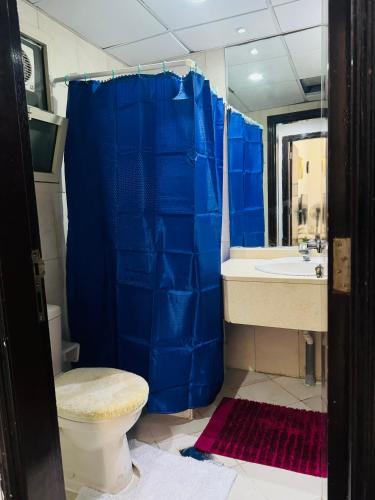 a bathroom with a blue shower curtain and a toilet at Cozy Dala Room in Sharjah