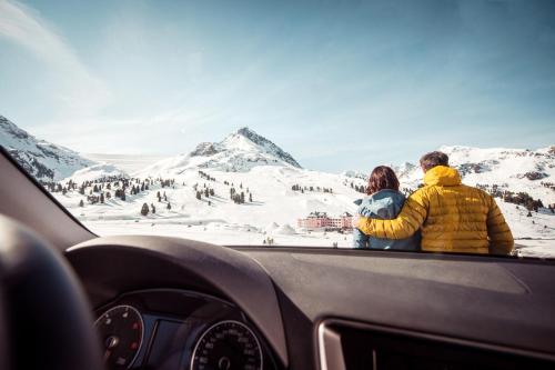 a man and woman sitting in a car looking at a snow covered mountain at Hotel Alpenrose aktiv & sport in Kühtai