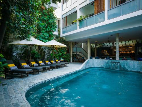 a swimming pool next to a building with chairs and umbrellas at Rambutan Resort – Phnom Penh in Phnom Penh