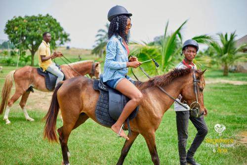 a woman riding a horse while a man walks behind her at Sogakope Beach Resort & Spa in Sogakofe