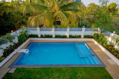 a pool in the backyard of a house with palm trees at Stayscape Abalone 6BHK Alibaug in Kīhīm