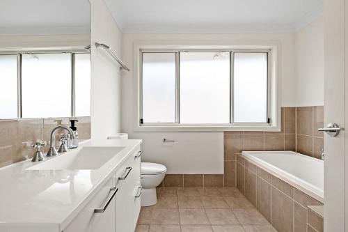 a white bathroom with a tub and a sink and a toilet at Luxe Ensuite Queen Room in Panania - Nearby Station in Panania