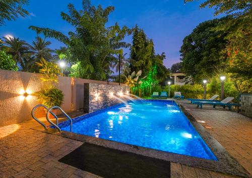 a swimming pool with a fountain in a backyard at night at Pop Tavern Kovalam Beach Villa by VOYE HOMES in Kovalam