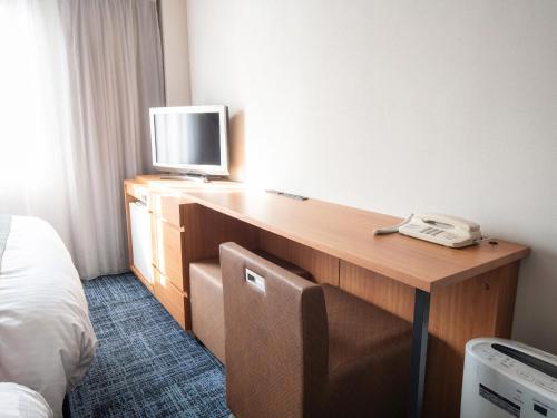 a hotel room with a desk with a television and a phone at Vessel Hotel Kurashiki in Kurashiki