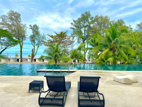 a swimming pool with two chairs and a table and some trees at By The Sea, Penang in Batu Ferringhi