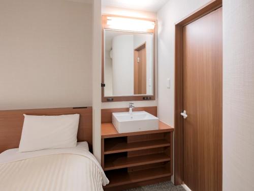 - une petite salle de bains avec un lavabo et un lit dans l'établissement Vessel Hotel Miyakonojo, à Miyakonojō