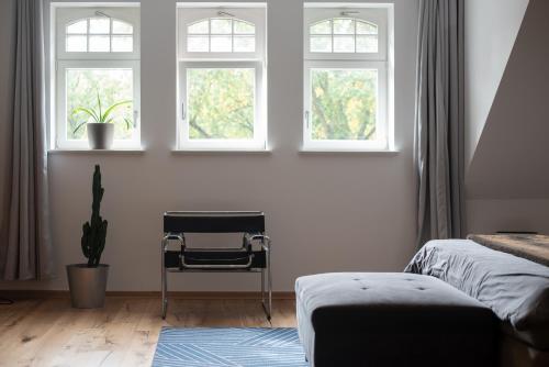 a bedroom with three windows and a chair in it at Apartment mit Parkblick & Massagestuhl in Leipzig
