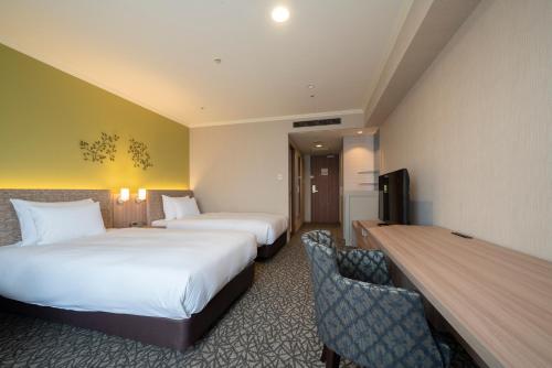 a hotel room with two beds and a desk at Hotel Associa Toyohashi in Toyohashi