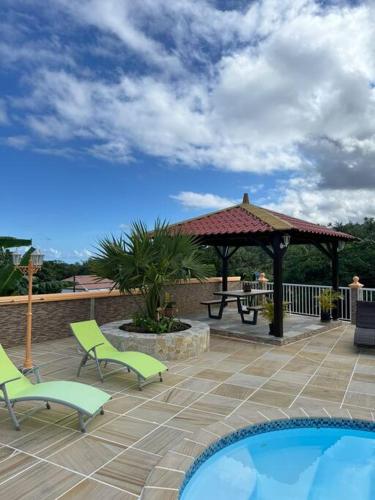 Un patio con un cenador y una mesa de picnic y sillas. en Le Volcan - Piscine - DODOTERLA, en Sainte-Rose