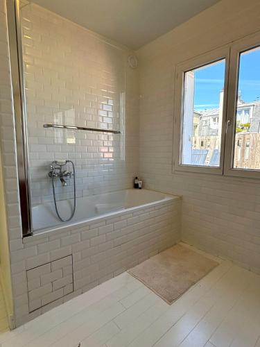 La salle de bains blanche est pourvue d'une baignoire et d'une fenêtre. dans l'établissement L'appartement Dagorno, à Paris
