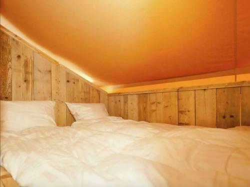 a large white bed in a room with wooden walls at Glamperen met eigen badkamer in De Peel voor 6 Pers Happy in Behelp