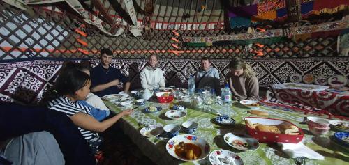 eine Gruppe von Menschen, die an einem Tisch mit Essen sitzen in der Unterkunft Yurt Stay Family Khansar in Nurota