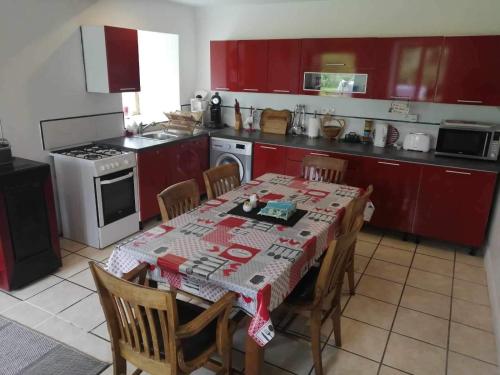 una cocina con mesa y sillas y una cocina con armarios rojos. en NormanD Holiday Home - VIRE CALVADOS Relaxing Rural Retreat, en Le Reculey